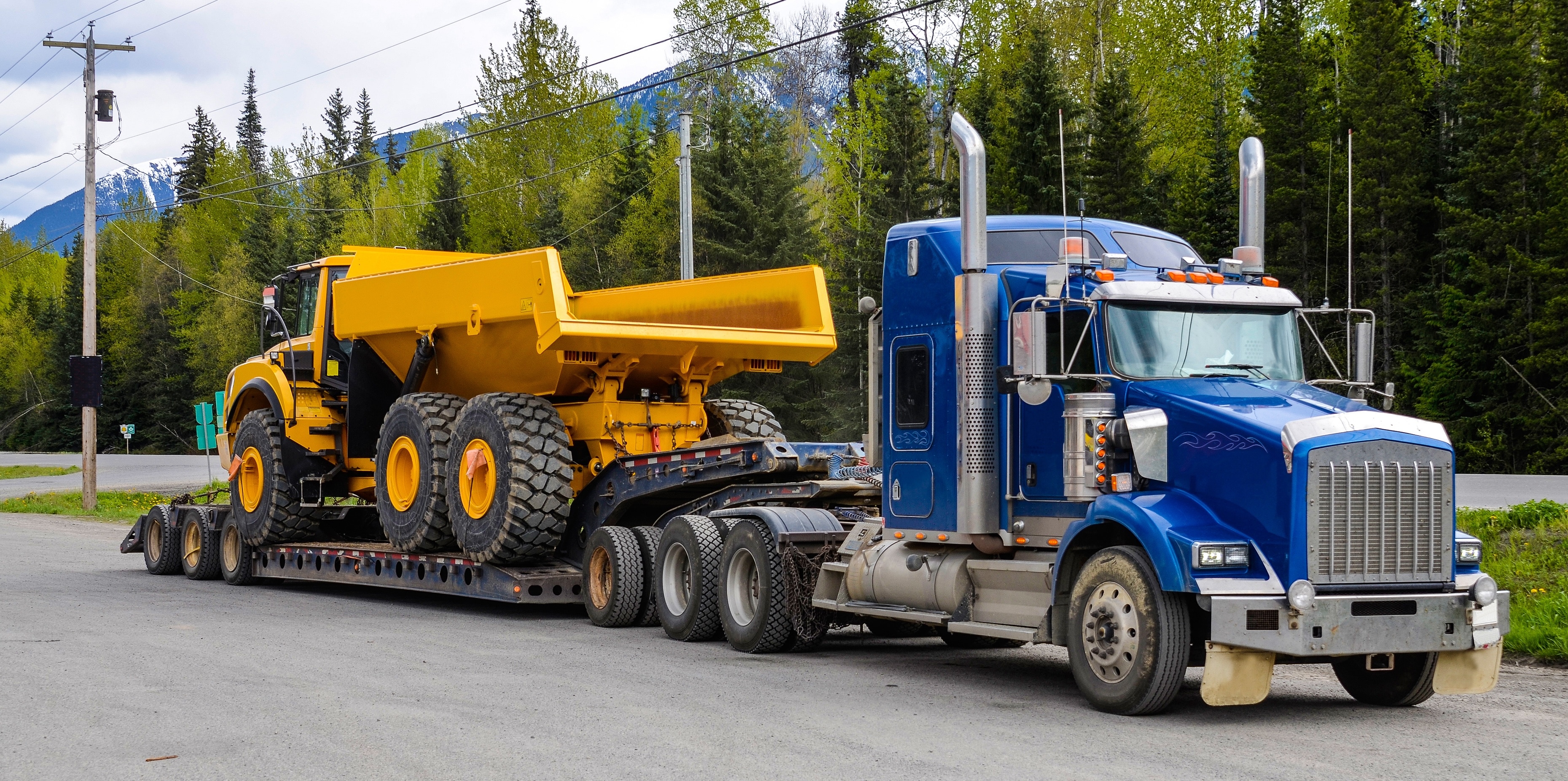 Big truck with a low platform trailer carrying a tipper truck on a public parking area of a truck stop