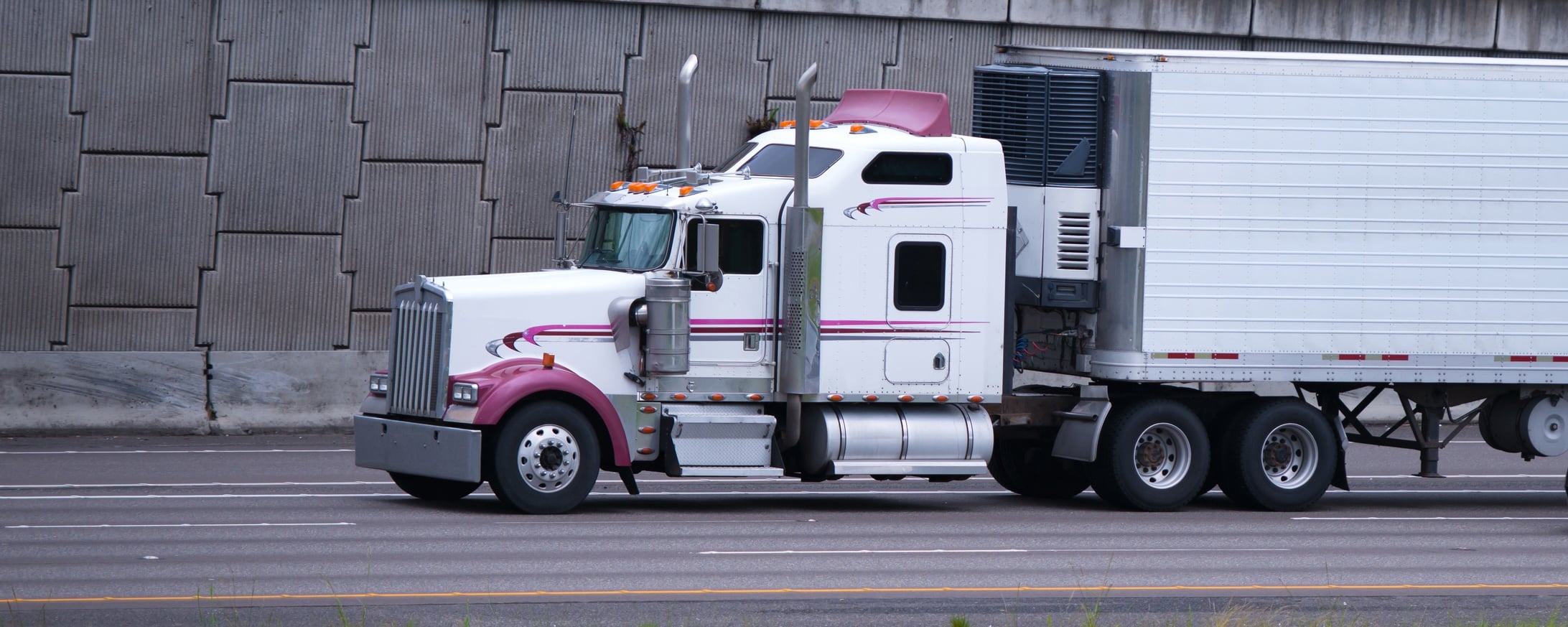 Classic big rig semi truck with color accents on fenders and spoiler and high tailpipes pulling a trailer with a refrigeration unit for the transport of perishable goods sensitive to temperature mode.